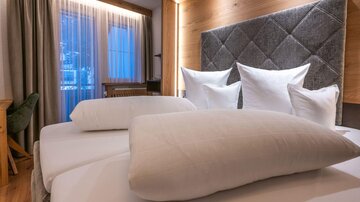 Ein gemütliches Schlafzimmer mit einem großen Bett und vielen Kissen. Das Design ist modern und einladend, mit warmen Holztönen und natürlichem Licht.