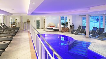 A modern spa with a blue pool and loungers. The area is designed to be bright and inviting.