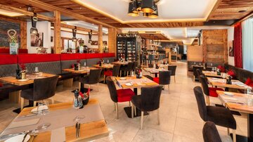 A modern restaurant with wooden elements and elegant table decorations. The seating areas are designed to be cozy and inviting.