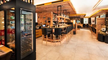 A modern bar with stylish wooden interior and an inviting atmosphere. In the background, there are shelves with beverages and seating for guests.