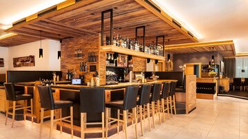 A stylish bar with wooden decor and comfortable chairs. The lighting creates a cozy atmosphere.