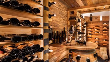 A cozy wine cellar with wooden shelves full of wine bottles. The warm atmosphere is enhanced by the wooden walls and the lighting.