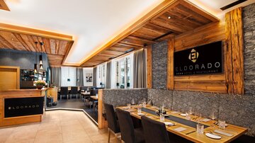 A modern restaurant with wooden paneling and elegant furnishings. The tables are set comfortably and the space feels inviting.