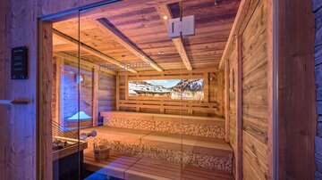 A modern sauna with wooden interiors and cozy benches. Through large windows, one can observe the beautiful mountain landscape.