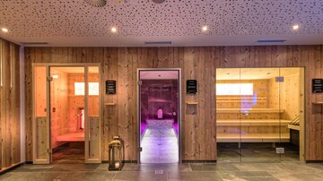 A relaxing wellness area with several saunas and a modern design. The walls are clad in wood, and soft lighting creates a calming atmosphere.