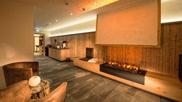 A cozy room with wooden paneling and a modern fireplace. Sofas and a small table invite you to relax.