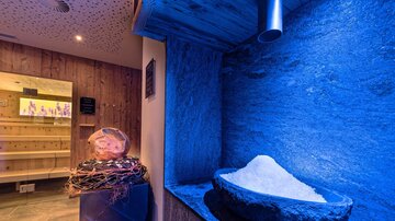 A wellness area with blue lights and a salt stone pool. In the background, a wooden sauna is visible.
