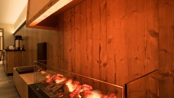 A modern fireplace with glowing logs in a stylish room. The wooden walls and soft lighting create a cozy atmosphere.