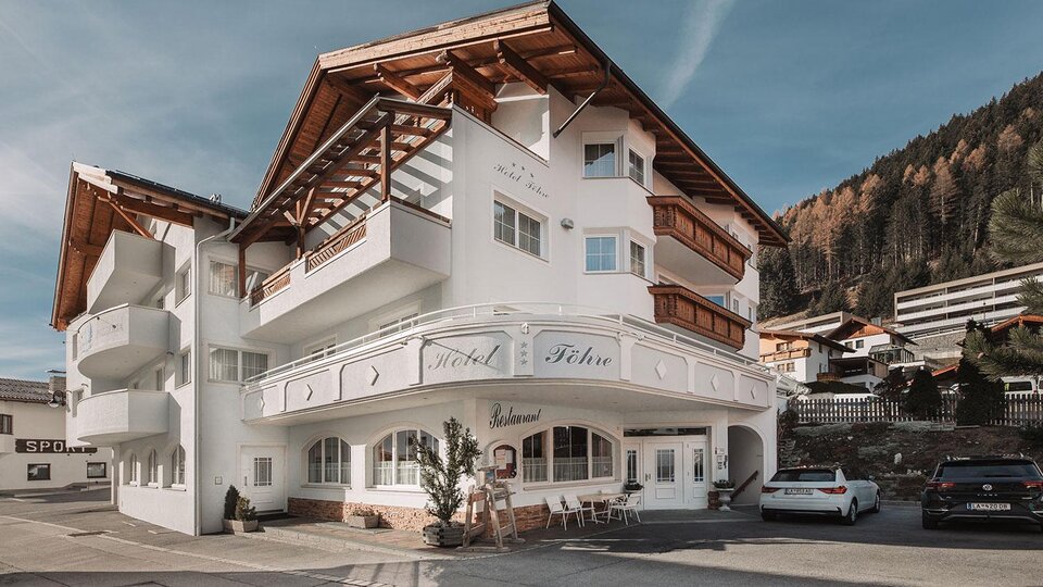 Ein gemütliches Hotel mit traditioneller Architektur und einem überdachten Balkon. Die Umgebung zeigt sanfte Hügel und Wald.
