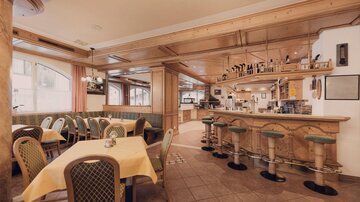 Ein einladendes Restaurant mit Holzinterieur und gemütlichen Tischen. Die Bar ist gut ausgestattet und der Raum wirkt freundlich und warm.