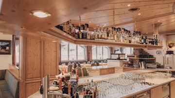 Eine stilvolle Bar mit einer großen Auswahl an Getränken und vielen Gläsern. Die Holzverkleidung und die gemütliche Atmosphäre schaffen einen einladenden Raum.
