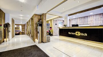 Ein modernes Hotel-Lobby mit Holzdetails und einem Empfangstresen. Der Empfang ist hell und einladend, mit dekorativen Pflanzen.