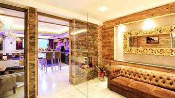 Ein modernes Wohnzimmer mit einer bequemen Couch und elegenen Holzelementen. Der Raum ist hell erleuchtet und verfügt über große Fenster.