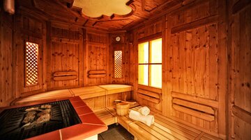 Eine gemütliche Sauna aus Holz mit Bänken und großen Fenstern. Sanftes Licht strömt herein und schafft eine entspannte Atmosphäre.