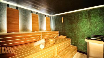 Eine moderne Sauna mit hellen Holzliegen und sanfter Beleuchtung. Die Wände sind in einem beruhigenden Grünton gestaltet.