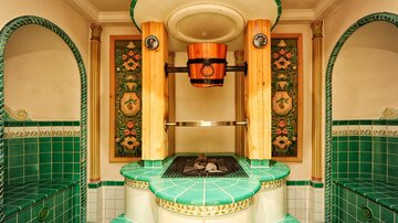 Ein eleganter Raum mit grünen Fliesen und dekorativen Wänden. In der Mitte befindet sich eine Sauna mit einem Holzofen und einer entspannenden Atmosphäre.
