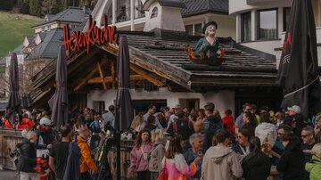 Ein belebtes Restaurant mit vielen Menschen vor dem Eingang. Über dem Eingang steht der Name des Lokals in roter Schrift.