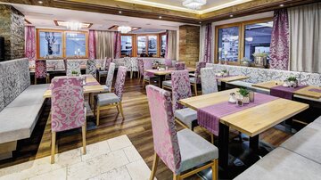 Ein modernes Restaurant mit stilvollen Tischen und gemütlichen Sitzecken. Die Atmosphäre ist hell und einladend, mit großen Fenstern und eleganter Dekoration.