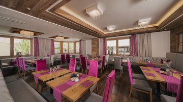 Ein modernes Restaurant mit hellen Holzelementen und bunten, pinken Stühlen. Große Fenster lassen viel Licht herein und schaffen eine freundliche Atmosphäre.