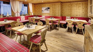 Ein gemütliches Restaurant mit holzverkleideten Wänden und roten Sitzbänken. Die Tische sind einfach dekoriert und schaffen eine einladende Atmosphäre.
