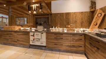 Eine warme und einladende Küche aus Holz mit rustikalem Charme. Auf der Arbeitsfläche stehen mehrere Kochutensilien und Geschirr.