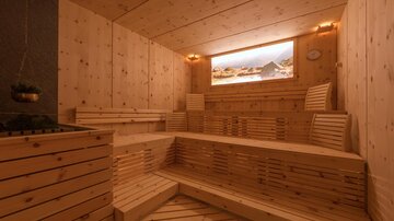 Eine moderne Sauna mit Holzelementen und mehreren Sitzbänken. Ein Fenster mit Blick auf eine Landschaft sorgt für eine entspannende Atmosphäre.