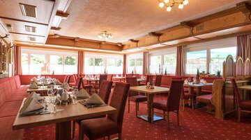 Ein gemütliches Restaurant mit roten Polstermöbeln und gedeckten Tischen. Große Fenster lassen viel Tageslicht hinein.