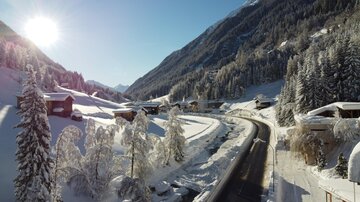Eine malerische Winterlandschaft mit schneebedeckten Bäumen und Häusern. Die Straße windet sich durch die verschneite Kulisse unter einem strahlend blauen Himmel.