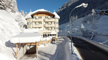 Ein charmantes Hotel im Schnee mit einem gut beschneiten Dach. Die Umgebung ist winterlich und malerisch mit einer ruhigen Straße.
