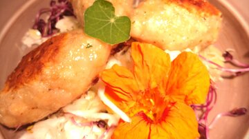 Ein Teller mit drei goldbraun gebratenen Knödeln, umgeben von frischem Sauerkraut und essbaren Blüten. Das Gericht ist ansprechend dekoriert und wirkt appetitlich.