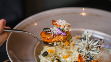 Ein Teller mit Risotto und gebratenen Garnelen ist zu sehen. Das Gericht ist mit essbaren Blüten und Kürbiskernen dekoriert.
