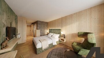 Ein modernes Hotelzimmer mit Holzverkleidung und einem großen Doppelbett. Eine stilvolle Ecke mit einem grünen Sessel und einem Fernseher ergänzt den Raum.