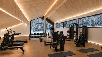 Ein modernes Fitnessstudio mit verschiedenen Trainingsgeräten und Matten. Große Fenster bieten einen Blick auf eine schneebedeckte Landschaft.