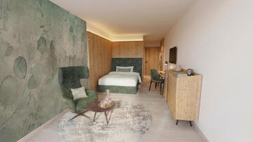 Ein modernes Zimmer mit einem Bett und einer bequemen Sitzecke. Die Wände sind in sanften Grüntönen gehalten und das Mobiliar ist aus hellem Holz.