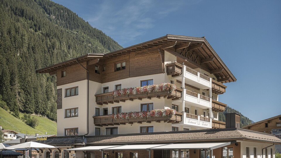 Ein hübsches Hotel mit einem traditionellen Holzdesign in einer malerischen Berglandschaft. Umgeben von grünen Bergen und Parkplätzen im Vordergrund.