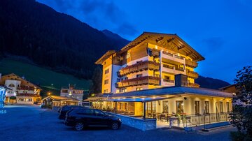 Ein hübsches Hotel in den Bergen, das abends beleuchtet ist. Umgeben von einer idyllischen Landschaft und Bergen.