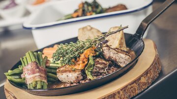 Ein köstliches Steak auf einer Pfanne, umgeben von grünen Bohnen und Gemüse. Die Präsentation ist rustikal und appetitlich.