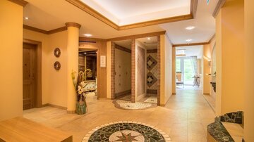 Ein heller und einladender Wellnessbereich mit warmen Farben und einem Mosaikboden. Im Hintergrund sind Sauna- und Duschbereiche sichtbar.