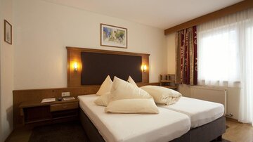 Ein gemütliches Zimmer mit zwei Einzelbetten und einem modernen Design. Große Fenster sorgen für viel Tageslicht und eine angenehme Atmosphäre.