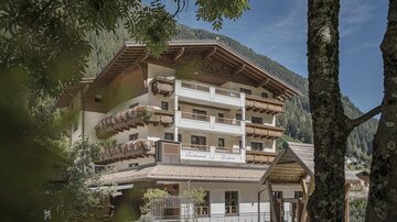 Ein charmantes Hotel in den Bergen mit traditionellen Holzbalustraden. Umgeben von Bäumen und einer schönen Landschaft.