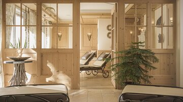 Ein gemütlicher Wellnessbereich mit Holzdetails und Liegen. Der Raum hat große Fenster und eine ruhige Atmosphäre.