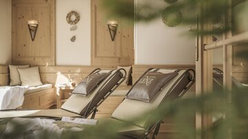 Ein entspannender Wellnessbereich mit Liegen, gemütlicher Holzverkleidung und sanftem Licht. Grünpflanzen verleihen dem Raum eine ruhige Atmosphäre.