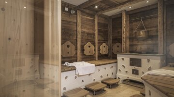 Eine gemütliche Sauna mit holzverkleideten Wänden und Sitzbänken. Es gibt eine harmonische Atmosphäre mit warmem Licht und traditionellen Sauna-Elementen.