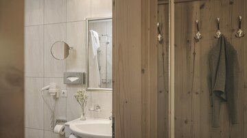 Ein modernes Badezimmer mit hellen Fliesen und Holzakzenten. Der Waschbeckenbereich ist gut organisiert und stilvoll eingerichtet.