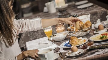 Ein elegantes Frühstück mit frischen Brötchen, Croissants, einem weichgekochten Ei und einem Glas Orangensaft. Die dekorierte Tischdecke und Kerzen schaffen eine gemütliche Atmosphäre.