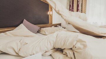 Ein ungemachtes Bett mit zerknitterter Bettwäsche und Kissen. Die Atmosphäre ist gemütlich und einladend.