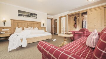 Ein komfortables Hotelzimmer mit einem großen Bett und gemütlichen roten Sofas. Die Wände aus Holz und die warme Beleuchtung schaffen eine einladende Atmosphäre.