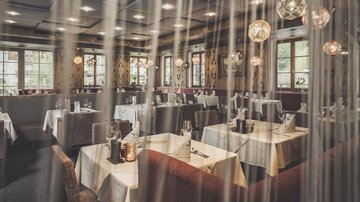 Ein elegantes Restaurant mit gedeckten Tischen und stilvoller Beleuchtung. Große Fenster lassen viel Tageslicht herein und schaffen eine einladende Atmosphäre.