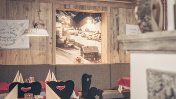 Ein gemütliches Restaurant mit Holzwänden und festlich gedeckten Tischen. An der Wand hängt ein großes Bild einer winterlichen Landschaft.
