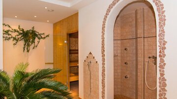 Ein elegantes Badezimmer mit einer Dusche im arabischen Stil. Im Hintergrund sind Pflanzen und ein Holzbereich zu sehen, die eine entspannende Atmosphäre schaffen.